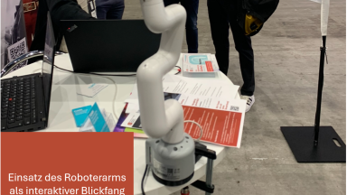 Ein weißer Roboterarm ist an einem Messestand auf einem Tisch befestigt. Der Roboterarm dient als interaktiver Blickfang und demonstriert automatisierte Bewegungsabläufe.