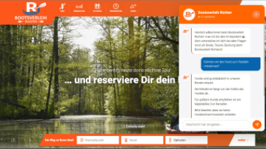 Screenshot der Website „Bootsverleih Richter“ mit eingeblendetem KI-Chatbot. Im Chat fragt ein Nutzer, ob Hunde zum Paddeln mitgenommen werden dürfen. Der Chatbot antwortet, dass Hunde grundsätzlich erlaubt sind, die Mitnahme von der Größe abhängt und für größere Hunde ein kippstabiles 3er-Kanadier empfohlen wird. Im Hintergrund ist eine bewaldete Flusslandschaft mit einem Kajak zu sehen.